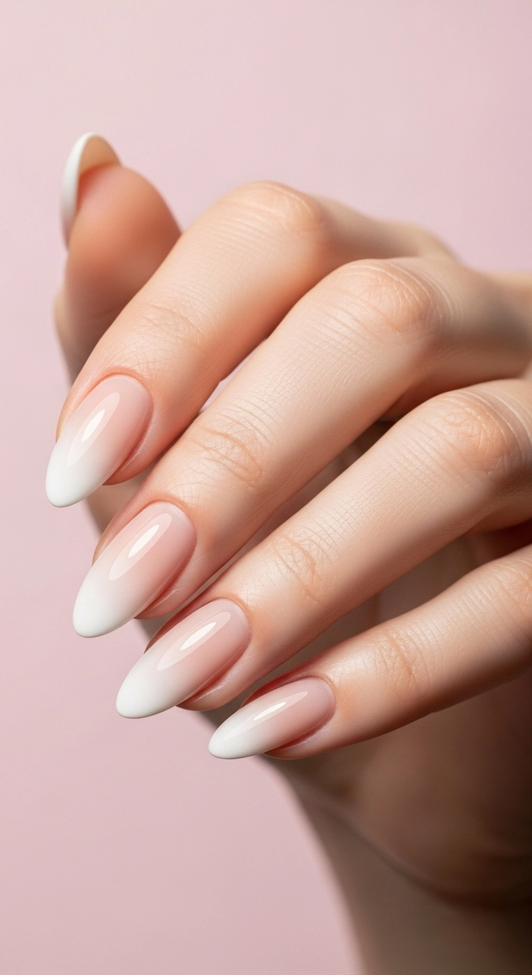 A soft and blended manicure showing an ombré or baby boomer effect, fading from a white tip to a nude base on almond nails.