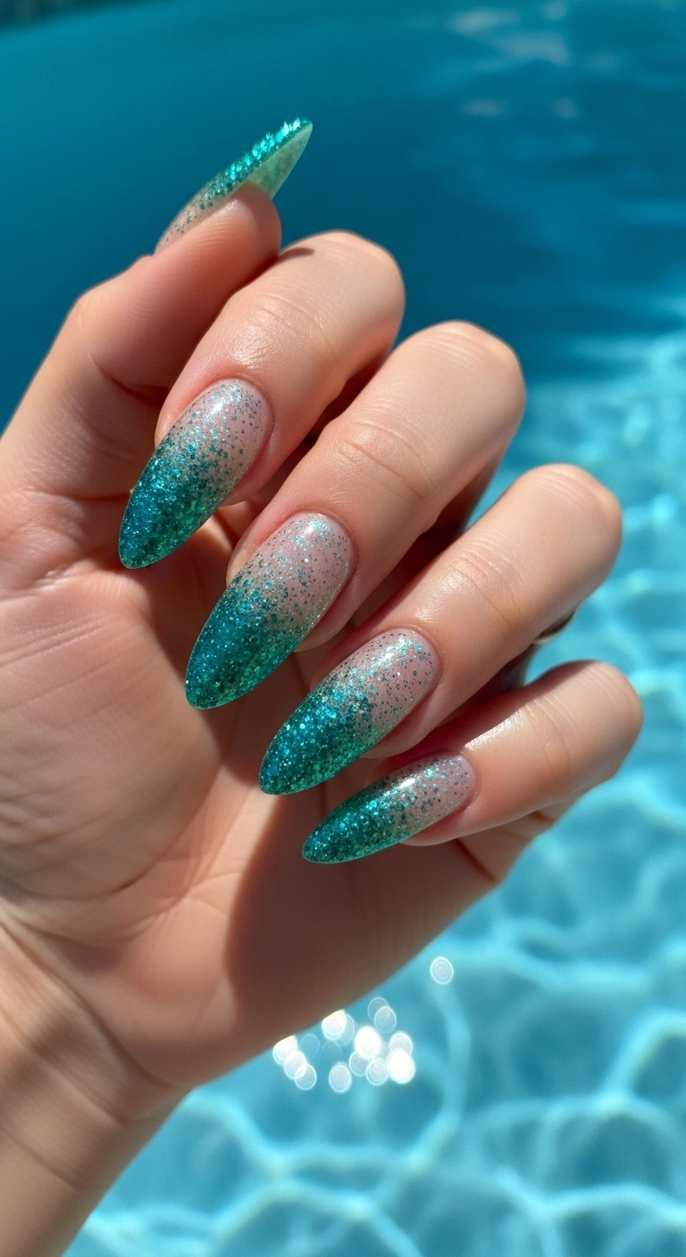 Almond nails with a sparkling turquoise glitter ombre effect, shimmering in the sun.