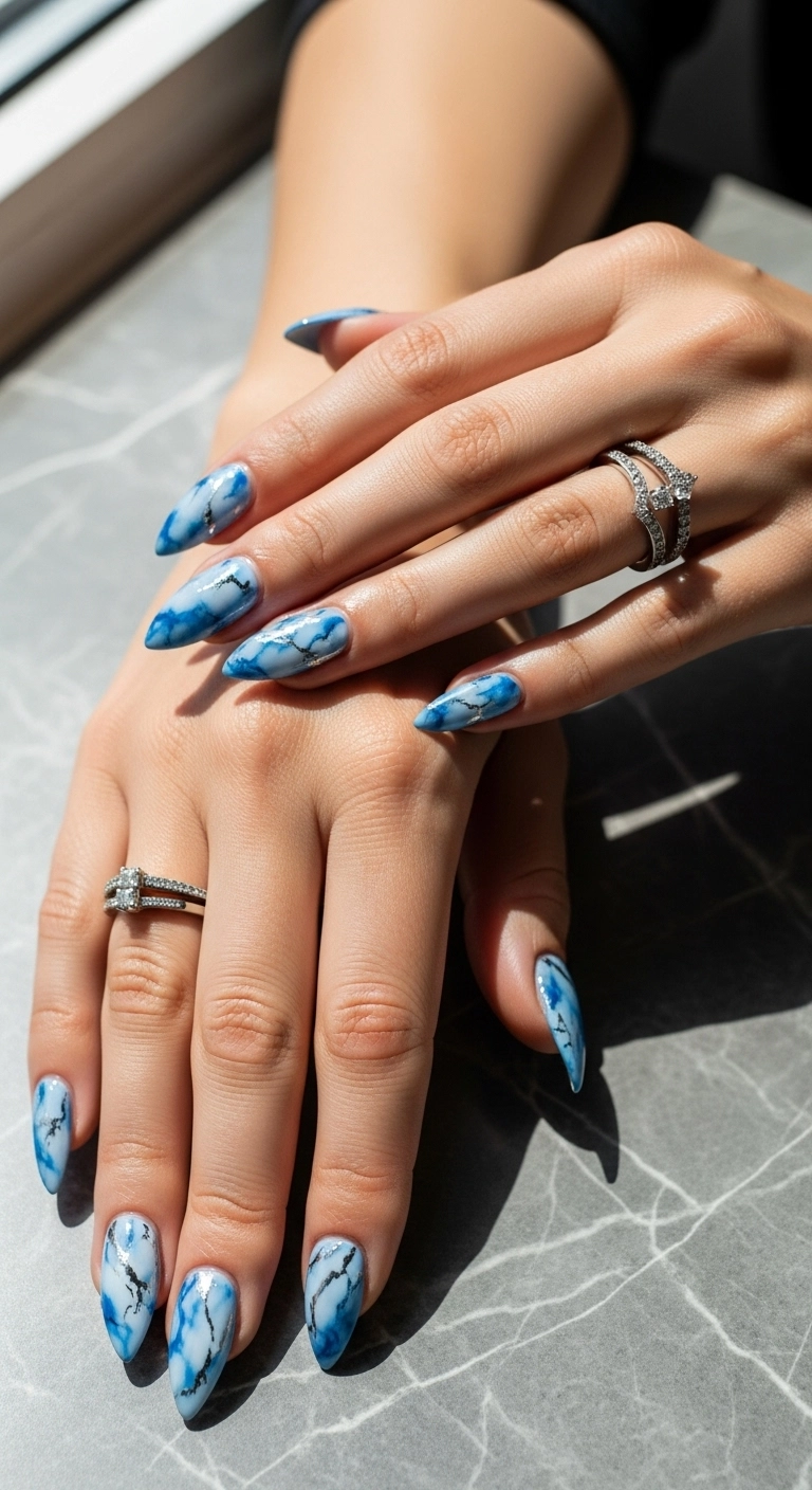 Long stiletto nails with a realistic blue and white marble effect and silver foil details.