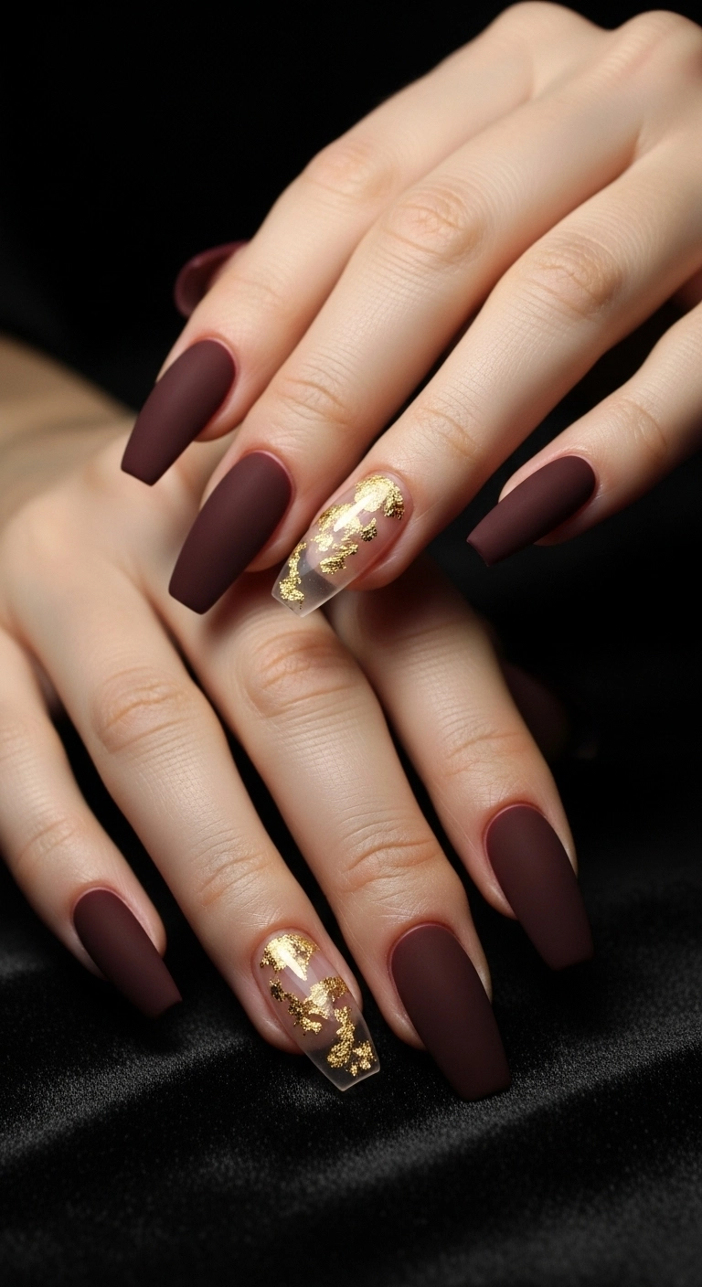 Long coffin acrylic nails in a matte deep burgundy color with gold leaf accent nails.