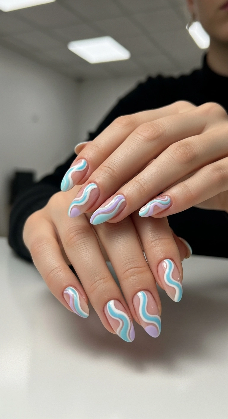 A close-up of almond-shaped gel nails with an abstract design of pastel blue, lavender, and white swirls on a nude base.