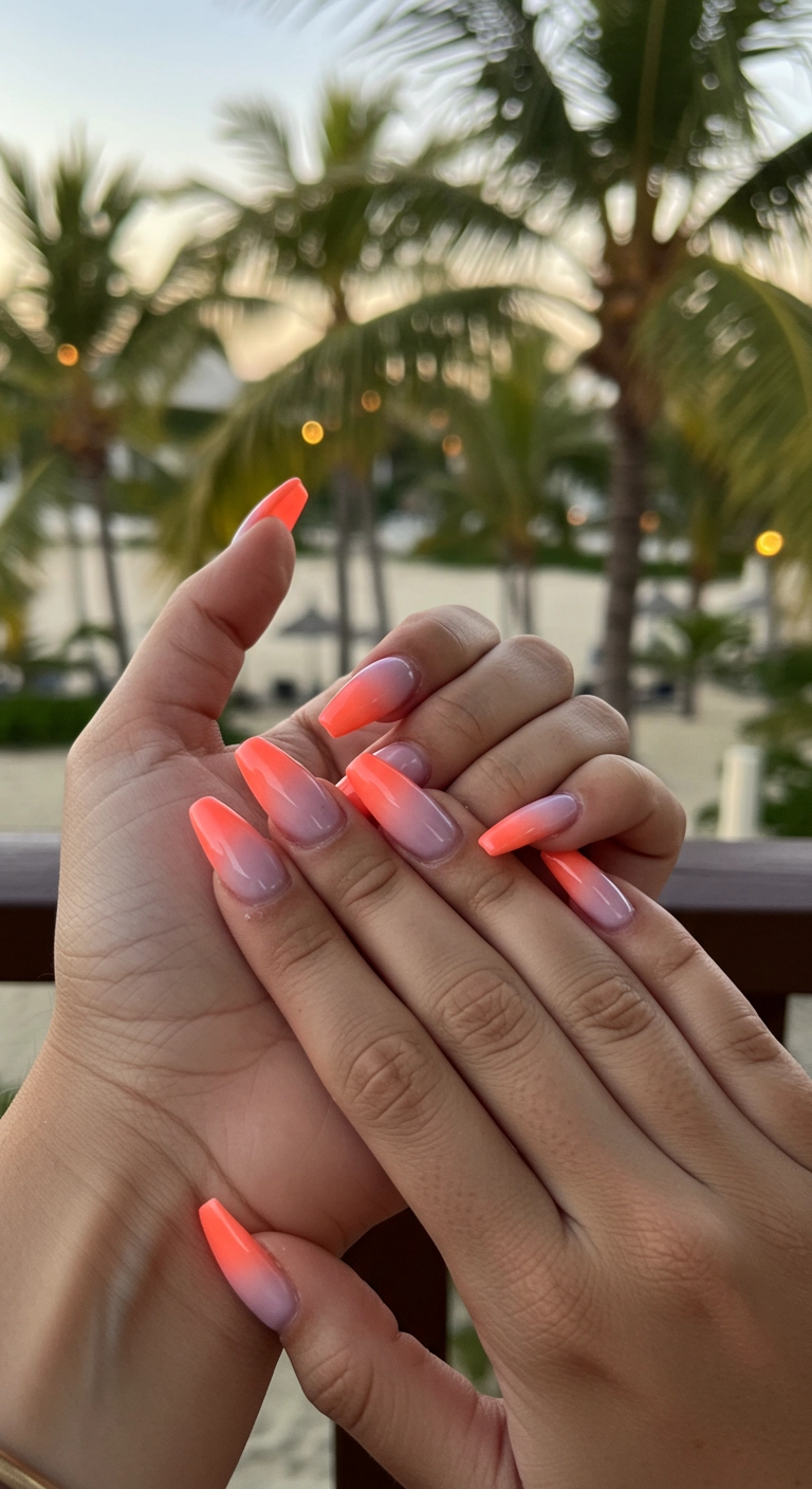 Close-up of almond-shaped nails with a coral to lavender sunset ombre design.