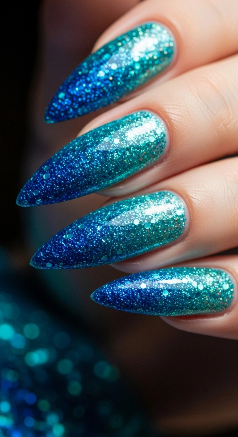 A close-up of stiletto nails with a deep blue and turquoise glitter ombré.