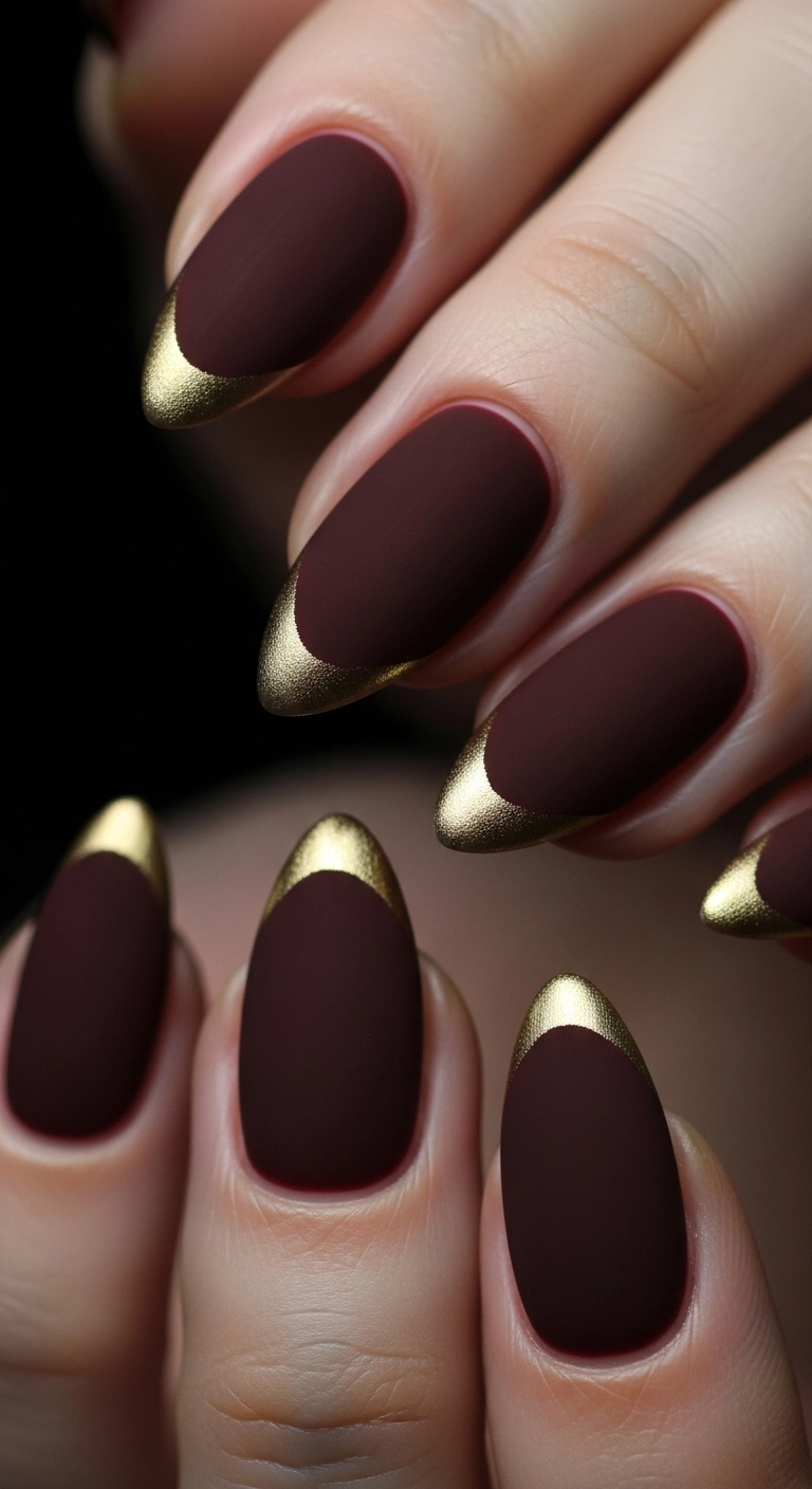 A macro shot of matte burgundy nails with a very thin, precise gold line tracing the cuticle.