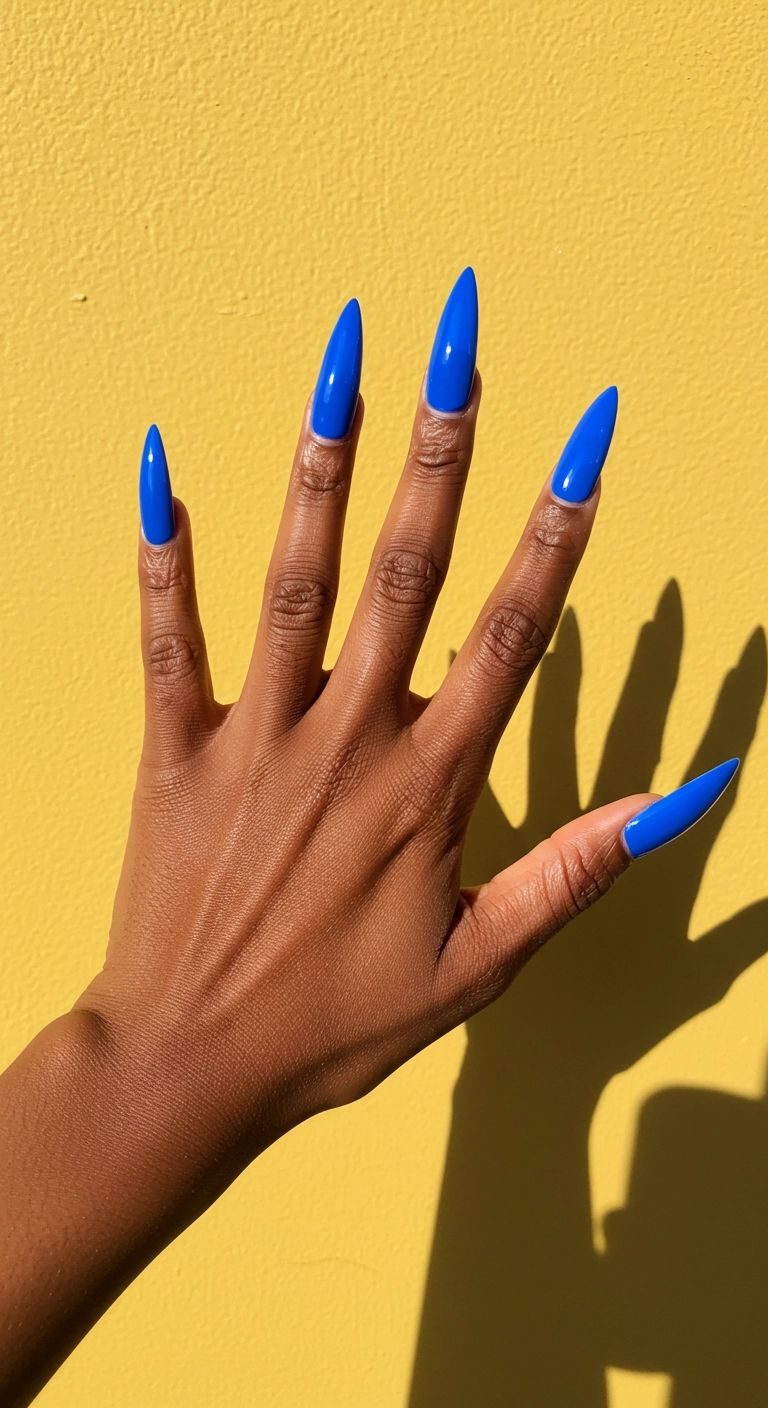 A hand with long, sharp stiletto nails painted in a vibrant, high-gloss electric blue polish.